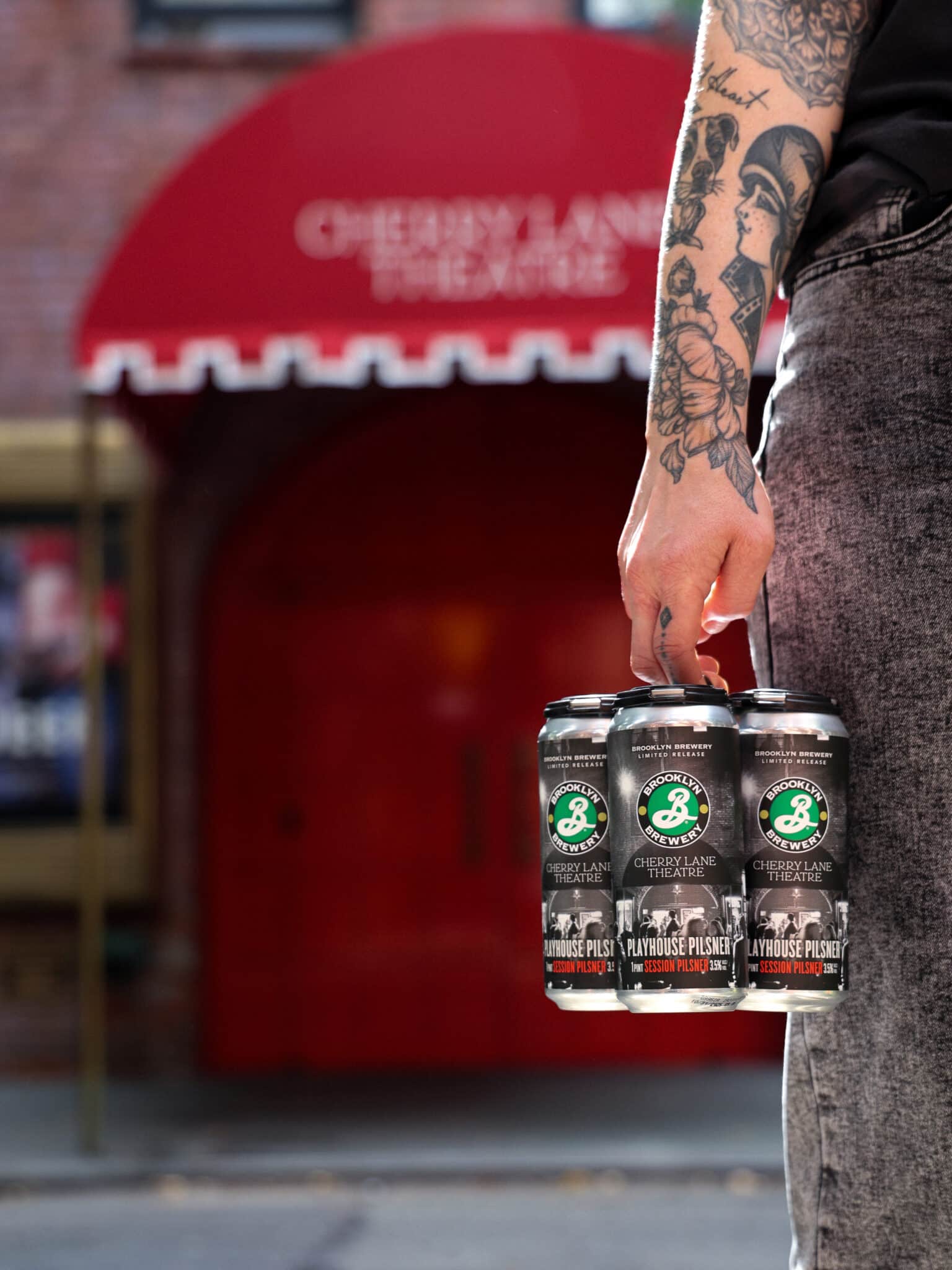 a person carrying a four pack of pilsner beer outside a theatre in new york city
